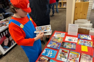 A kid dressed as Mario browses a table full of free comic books on free comic book day