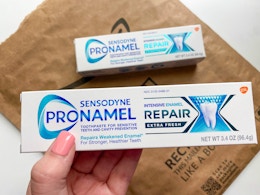 a hand holding a box of toothpaste over an Amazon mailer