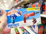 hand holding a nerf fortnite blaster set in front of a target shelf