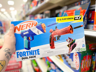hand holding a nerf fortnite blaster set in front of a target shelf
