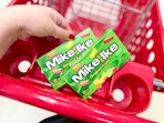 hand holding a box of mike & ike candy over a target cart