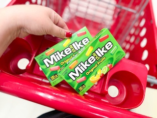 hand holding a box of mike & ike candy over a target cart