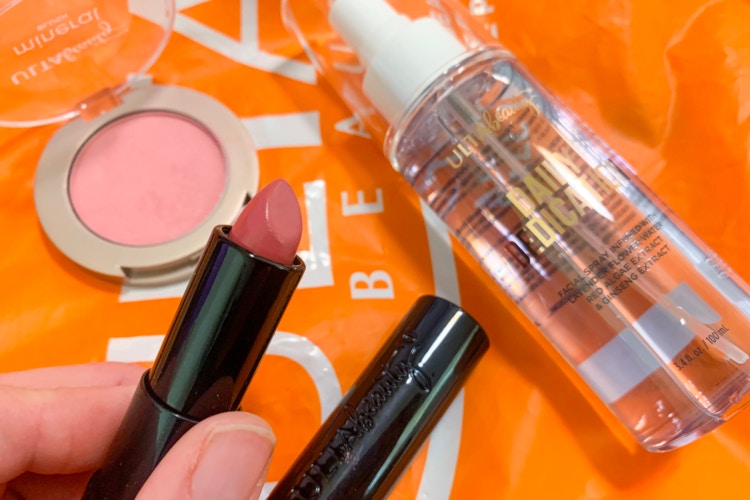 Hand holding lipstick, overtop blush and facial spray on top of an orange Ulta bag