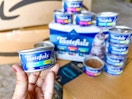 can of cat food stacked on Amazon boxes and a hand holding a can