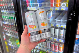person holding 2 celsius energy drinks in front of a cooler