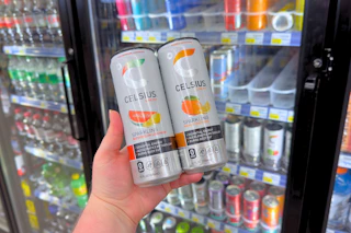 person holding 2 celsius energy drinks in front of a cooler