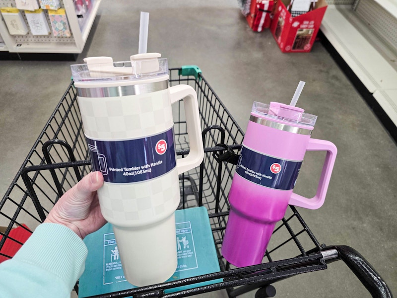 person holding a tan tumbler over a cart with a pink tumbler in it