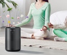 a person sitting on a yoga mat next to an air purifier 