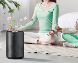 a person sitting on a yoga mat next to an air purifier 