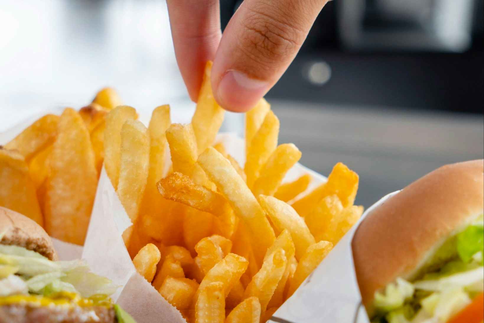 A person's hand reaching down to take a fry from a bag of french fries from Fatburger.
