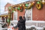 man using pole to hang up Christmas lights