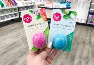 A hand holding up eos lip balm in a store aisle.