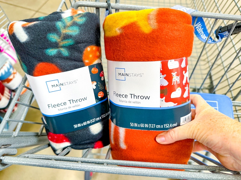 hand holding a mainstays fall fleece throw with another throw in walmart cart