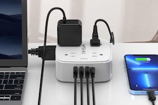 An 8-outlet surge protector sits on a desk between a laptop and a smart phone.