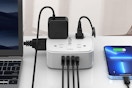 An 8-outlet surge protector sits on a desk between a laptop and a smart phone.