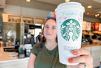 a woman wearing a birthday crown holding out a venti starbucks coffee cup with Happy Birthday written on cup 