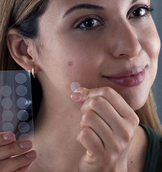 a woman putting a pimple patch on her face