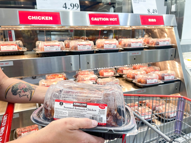 a person holding a rotisserie chicken putting in a cart at costco