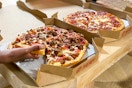 a person grabbing a piece of Pizza Hut pizza from a pizza box on a table.