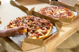 a person grabbing a piece of Pizza Hut pizza from a pizza box on a table.