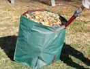 a hand pulling a green bag full of leaves in a yard