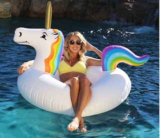 A woman sitting in a unicorn pool float in the pool