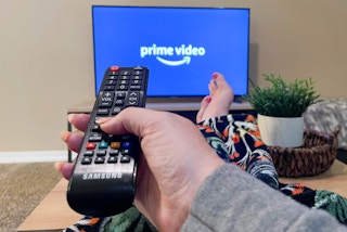A person sitting on a couch with their feet up, pointing a remote at a TV with the Prime Video TV app's start-up screen displayed.