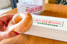 someone holding a Krispy Kreme donut in front of a Krispy Kreme box