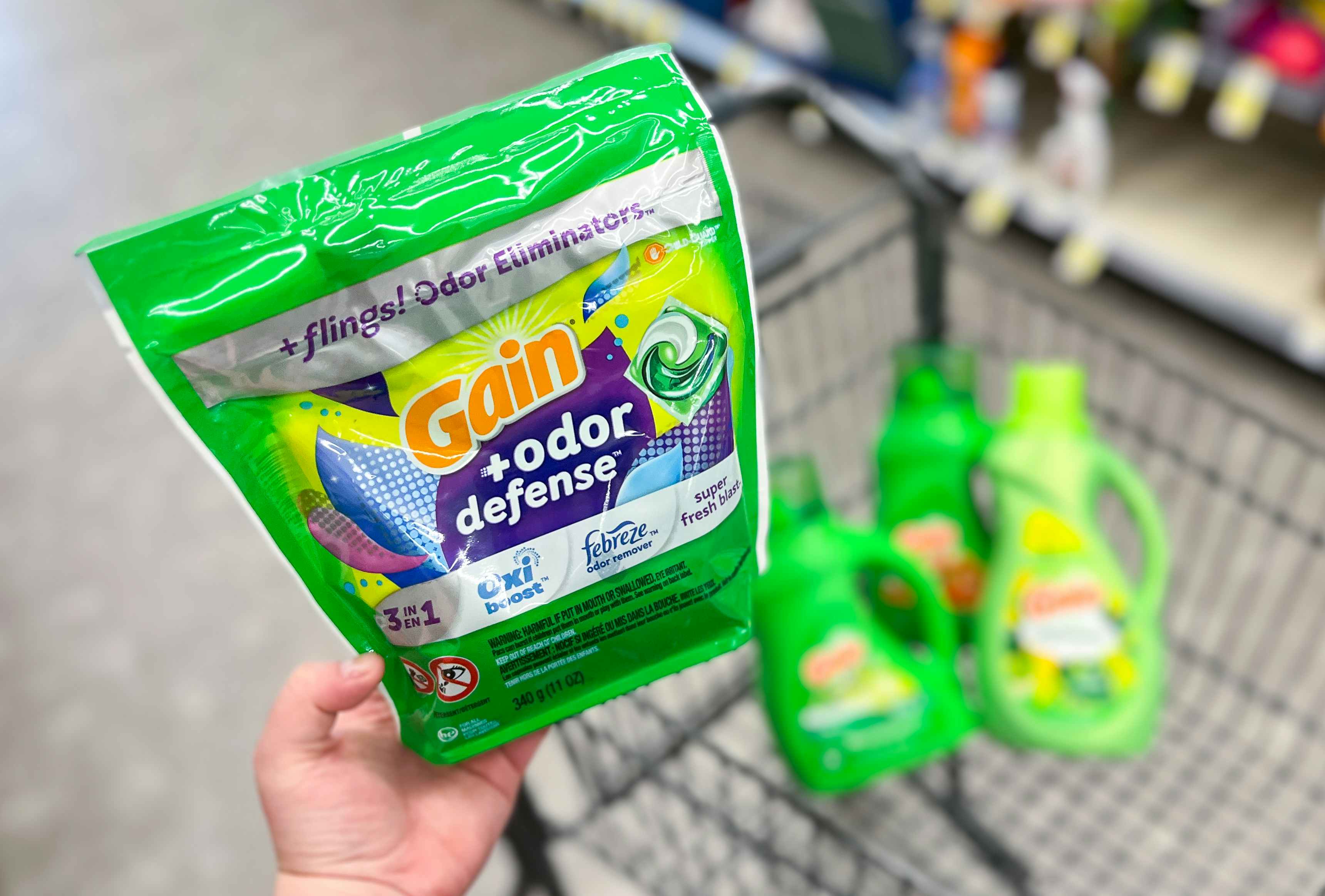 hand holding gain flings laundry detergent with walgreens cart holding more gain laundry care