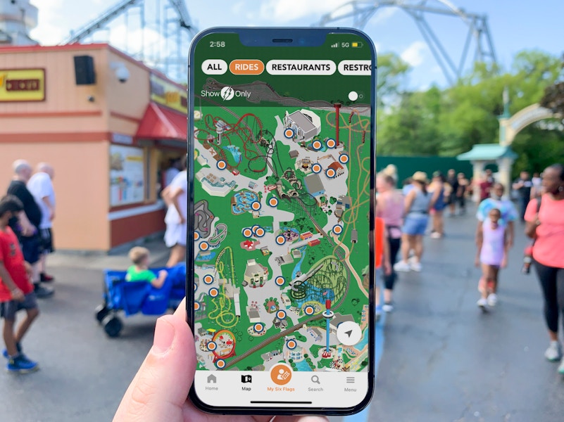 Rides section of the Six Flags up, on a phone screen, held up with the park in the back.
