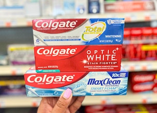 hand holding three tubes of Colgate toothpaste