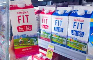 hand holding a carton of Darigold FIT whole milk in front of the refrigerated aisle