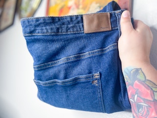 A person's hand holding up a pair of Madewell jeans in their home.