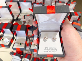 someone holding a pair of stud earrings in a red and black box