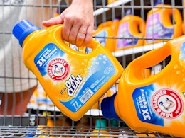hand holding a bottle of arm & hammer detergent next to another bottle in walmart cart