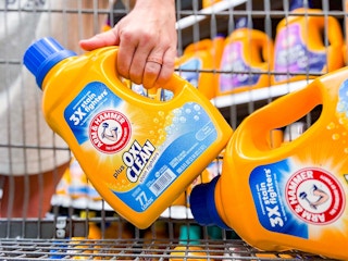 hand holding a bottle of arm & hammer detergent next to another bottle in walmart cart