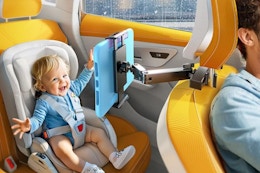 A baby sits in the back seat in a carseat, looking happily at a tablet on the arm of the tablet holder, which is attached to the headrest