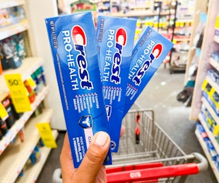 hand holding three crest pro health toothpaste inn front of cart