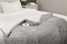 Lifestyle image of Sunbeam electric blanket (grey quiled) draped over bed corner
