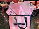 A Victoria's Secret gift card sticking out of a shopping bag filled with pink tissue paper.