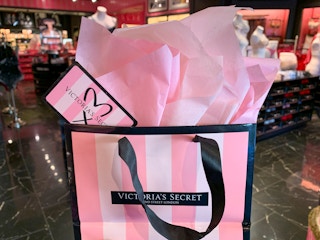A Victoria's Secret gift card sticking out of a shopping bag filled with pink tissue paper.