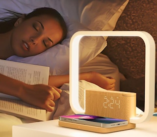 a clock charger on a nightstand next to a person in asleep in bed