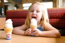 Little girl licking and ice cream cone sitting at a booth in Dairy Queen