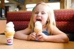 Little girl licking and ice cream cone sitting at a booth in Dairy Queen