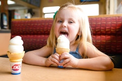 Little girl licking and ice cream cone sitting at a booth in Dairy Queen
