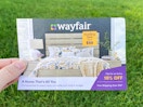 a hand holding the edge of a wayfair mailer coupon for 10% off