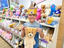 A kid holding up a pre-stuffed Birthday bear at Build-A-Bear