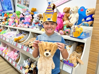 A kid holding up a pre-stuffed Birthday bear at Build-A-Bear