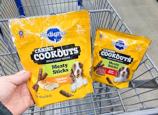 hand holding a Pedigree Canine Cookouts dog treats in front of another packing in a Walmart cart
