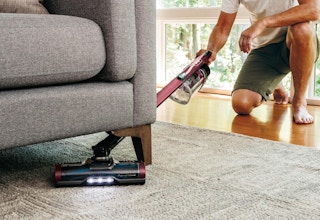 a person vacuuming with a stick vacuum under a couch